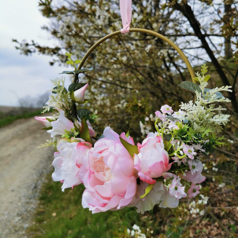 Künstlicher Blumenkranz mit Pfingstrosen rosa an Deko goldring hängt am Baum in der Natur