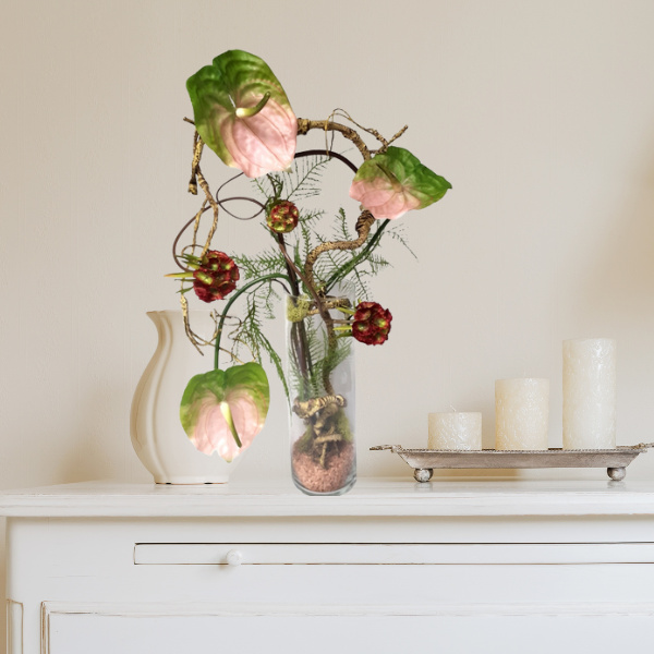 Rosa Anthurien Kunstblumengesteck im Glas Zylinder mit braunen Dekosteinen dekoriert und Kerzen stehen auf Kommode weiss