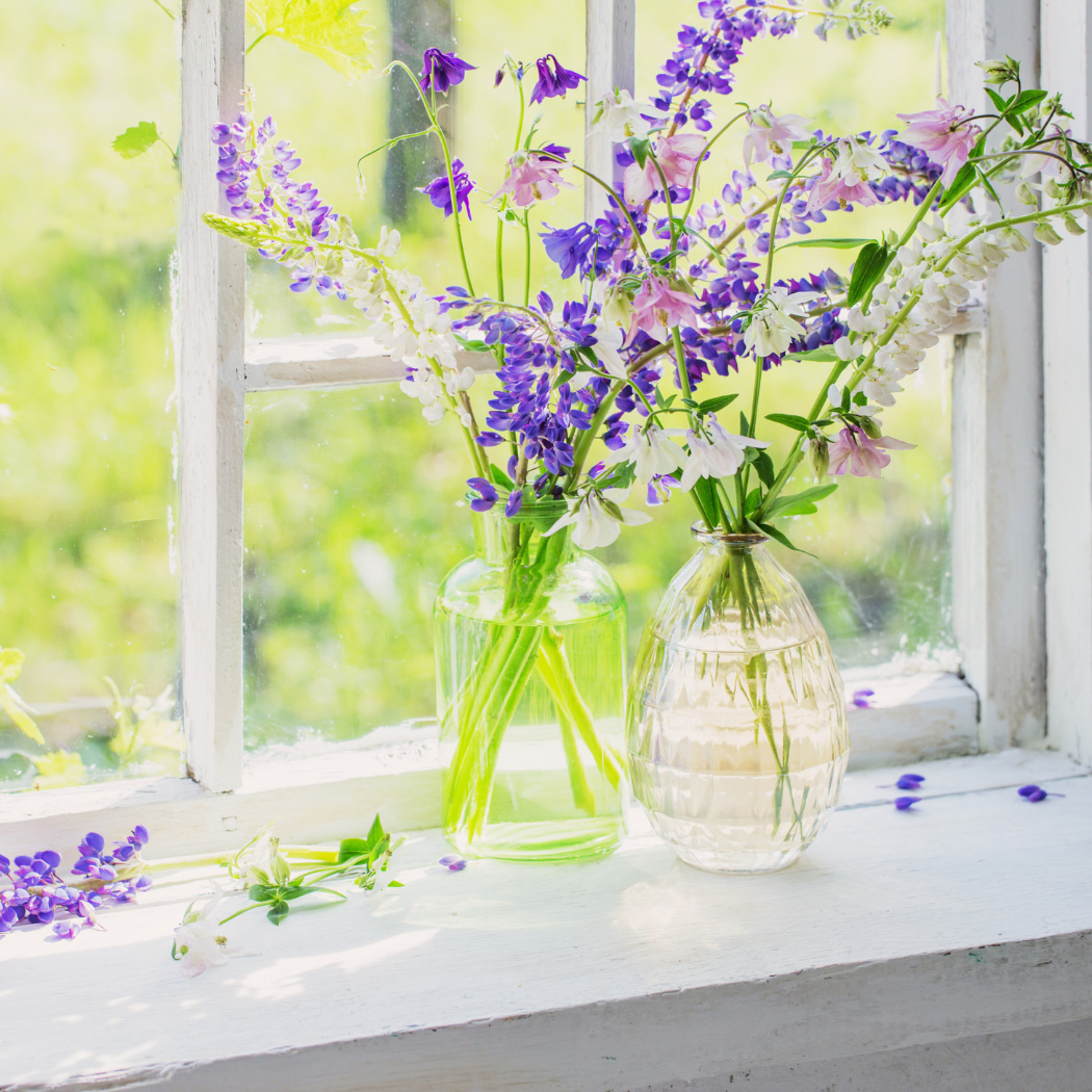 künstliche Gartenblumen Wicken violett und Cosmea Blüten weiß in Glasvase auf Tisch