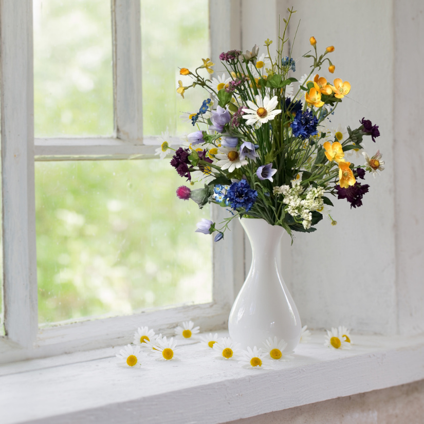 Weiße Keramikvase mit künstlichen Feldblumenstrauß auf Fensterbank
