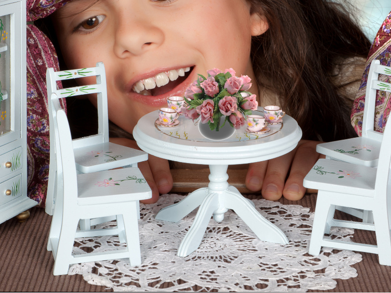 Kind schaut ins Puppenhaus auf Esstisch mit kleinen Kunstblumenstrauß mit rosa Rosen