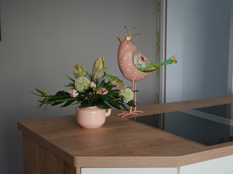 Deko Metall Vogel rosa mit gold Krone neben Kunstblumenstrauß auf Küchenarbeitsplatte
