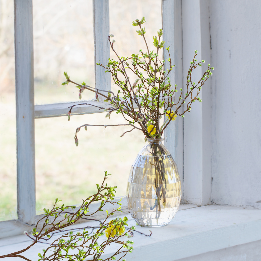 künstliche Zweige gelb in Glasvase am Fenster auf Fensterbank dekoriert