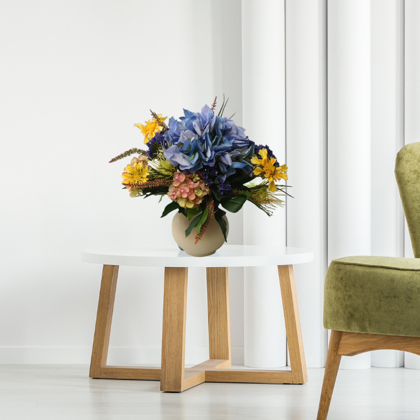 Kunstblumenstrauß flach gebunden mit Hortensien blau und Sonnenhutblüten in Vase auf Tisch