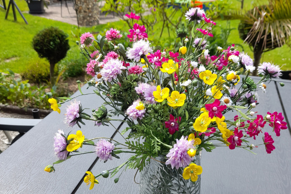 Bunder Wiesenblumenstrauß mit künstlichen Butterblumen Klee und Kamille Blüten in Glasvase auf Holztisch